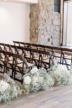 a row of wooden chairs with white flowers on the floor in front of an open stone wall