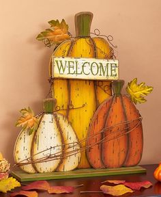 a wooden welcome sign with pumpkins and leaves around it on top of a table