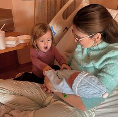 a woman holding a baby while sitting on top of a bed next to another person