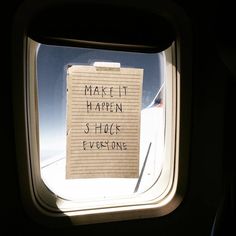 a sticky note attached to the side of an airplane window that says make it happen shock everyone