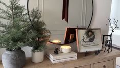 a wooden table topped with two vases filled with plants and candles next to a mirror