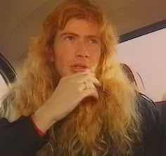 a man with long blonde hair sitting in the back seat of a car and holding his hand to his mouth