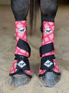 the legs and feet of a horse wearing pink boots with black straps, standing in sand