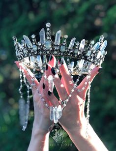 two hands holding up a tiara with crystal beads and crystals on the sides, in front of some trees