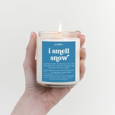 a hand holding a candle that says i smell snow on the front and back of it