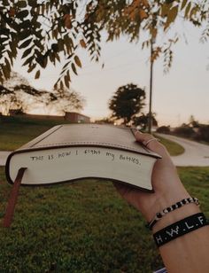 a hand holding an open book with writing on it in front of a grassy field