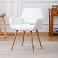 a white chair sitting on top of a wooden floor next to a table and lamp