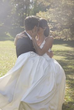 a bride and groom are kissing in the park on their wedding day with sunlight streaming through the trees behind them