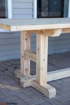 a wooden table sitting on top of a brick floor next to a building with windows