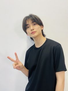 a young man standing in front of a white wall making the peace sign with his fingers