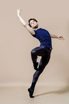 a man in blue shirt and black pants standing on one leg with his arms out