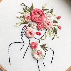 a woman's face with flowers in her hair is embroidered onto a white piece of fabric