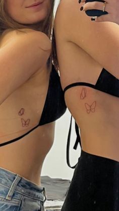 two women with tattoos on their backs taking a selfie in front of a mirror