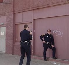 two police officers standing in front of a garage door with graffiti on the wall behind them