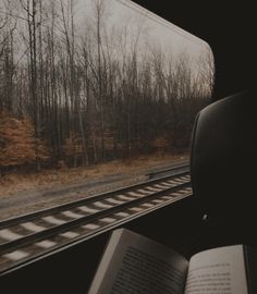 an open book sitting on top of a seat next to a train track with trees in the background