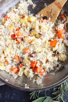 rice with carrots and other vegetables in a pan on the stove top next to a wooden spoon