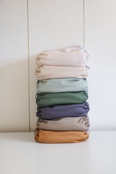 folded cloths stacked on top of each other in different colors and sizes, sitting on a white surface