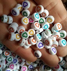 a hand is full of heart shaped beads in white and multicolored hearts on the palm