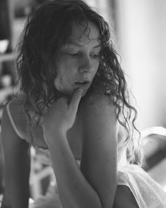 a young woman sitting on top of a bed with her hand under her chin and looking down