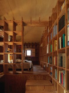 there are many bookshelves in the room with wooden shelves on each side and a bed behind them