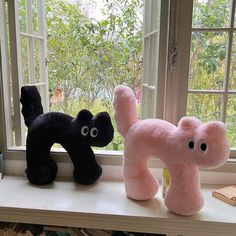 two black and pink stuffed animals sitting on a window sill next to each other