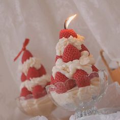 two small red and white strawberries in a glass bowl with a lit candle on top