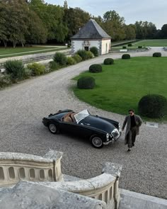 a man standing next to a black car on top of a gravel road in front of a building