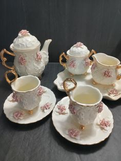 four tea cups and two saucers with pink flowers on them, all in gold trimmings