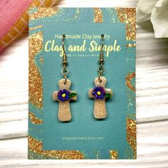 a pair of earrings with flowers in the shape of a cross on top of a card