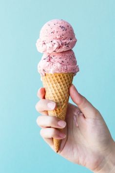 a hand holding an ice cream cone with pink icing