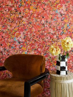 a chair and vase with flowers in front of a colorful wallpapered room area