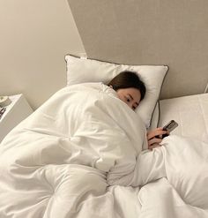 a woman laying in bed under a blanket with a cell phone next to her head