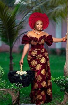 an african woman in a red dress and head wrap holding a palm tree with her hand