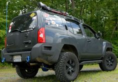 the rear end of a gray four door suv parked in front of trees and bushes