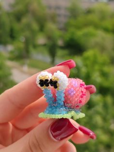 a hand holding a small beaded object in it's palm with trees in the background