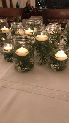 candles are lit in glass jars with greenery on the table