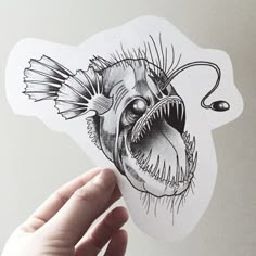 a hand holding up a sticker with an image of a fish in it's mouth