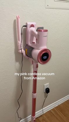 a pink cordless vacuum is plugged into the wall with an alarm clock on it