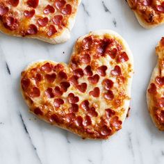 four heart shaped pizzas sitting on top of a white marble counter topped with cheese and pepperoni