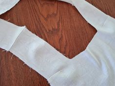 a piece of white fabric is cut in half on top of a wooden table with scissors