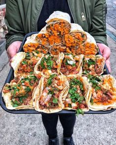 a person holding a tray full of tacos