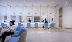 a woman sitting on a blue chair in front of a white counter with people behind it