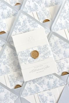 a wedding card with a wax seal on it surrounded by white envelopes and gold buttons