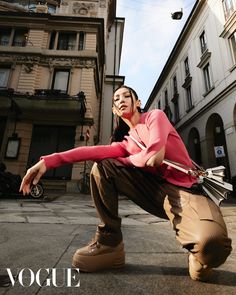 a woman in pink shirt and brown pants crouching on the ground