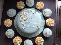 a birthday cake surrounded by cupcakes and flowers