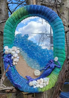 a blue and green wicker frame with shells on it, in front of a tree