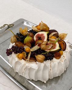 a cake with fruit on it sitting on top of a metal tray next to a knife and fork