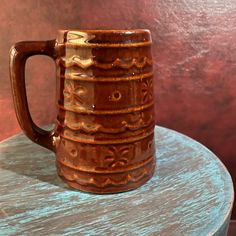 a brown coffee mug sitting on top of a wooden table next to a red wall