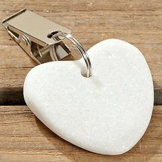 a white heart shaped keychain with a metal clip attached to it on a wooden surface