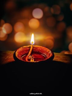 a lit candle sitting on top of a wooden table with blurry lights in the background